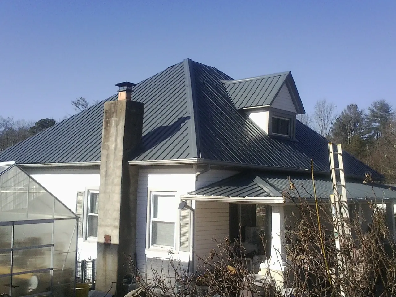 Dark blue standing seam metal roof on a white farmhouse with dormer — Slate & Tile Roof Repair by Roofing Brothers in North Tonawanda
