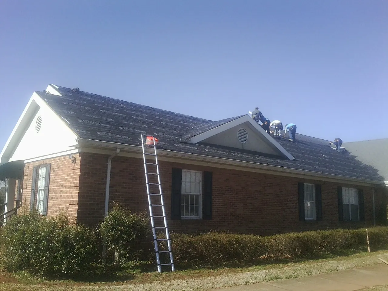 Crew tearing shingles off a brick ranch roof with a ladder set — Emergency Roof Repair work by our crew in North Tonawanda