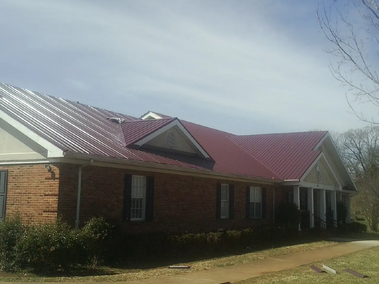 Red metal roof with gabled entries on a long brick building, from a Hail Damage Roof Repair job in North Tonawanda