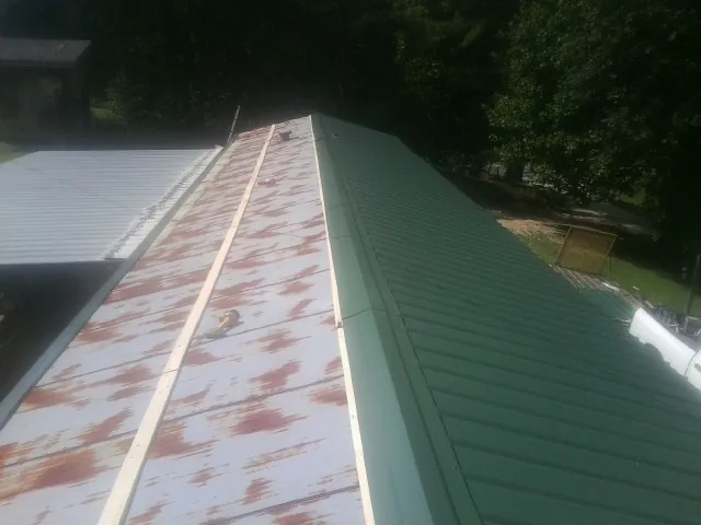 Old rusted panels beside newly installed green metal roofing — Wind Damage Roof Repair by Roofing Brothers in North Tonawanda