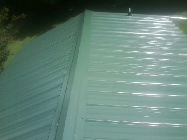 New green metal panels meeting at the ridge of a roof — Flat Roof Repair work by our crew in North Tonawanda