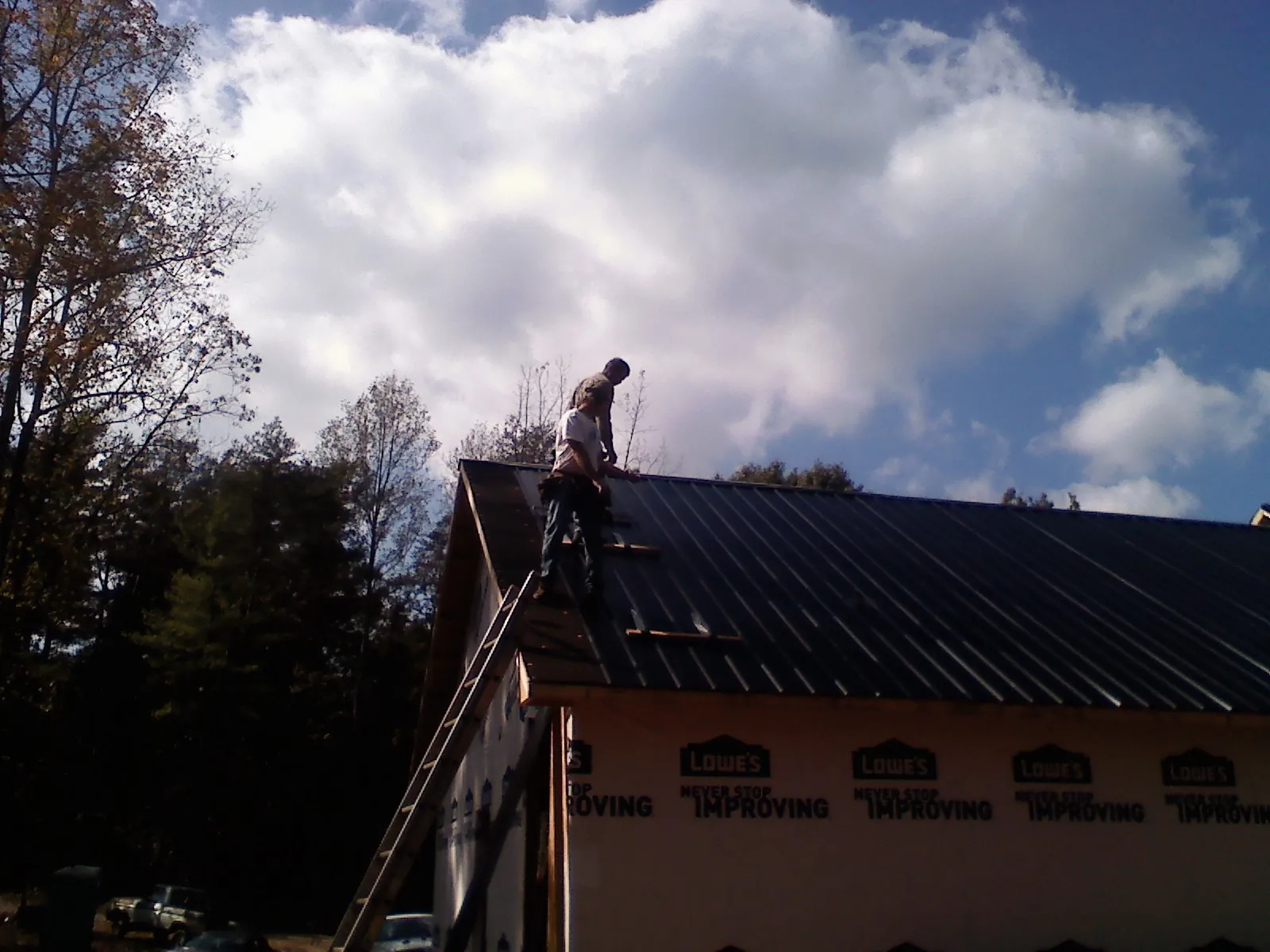 Roofer fastening dark metal panels high against a cloudy sky, from a Roof Inspection job in North Tonawanda