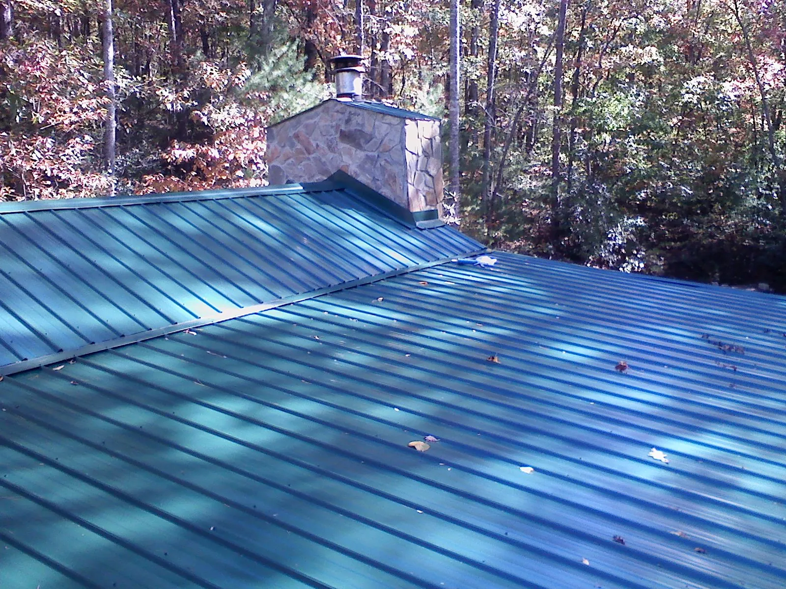 New green metal roof and stone chimney surrounded by autumn woods in North Tonawanda