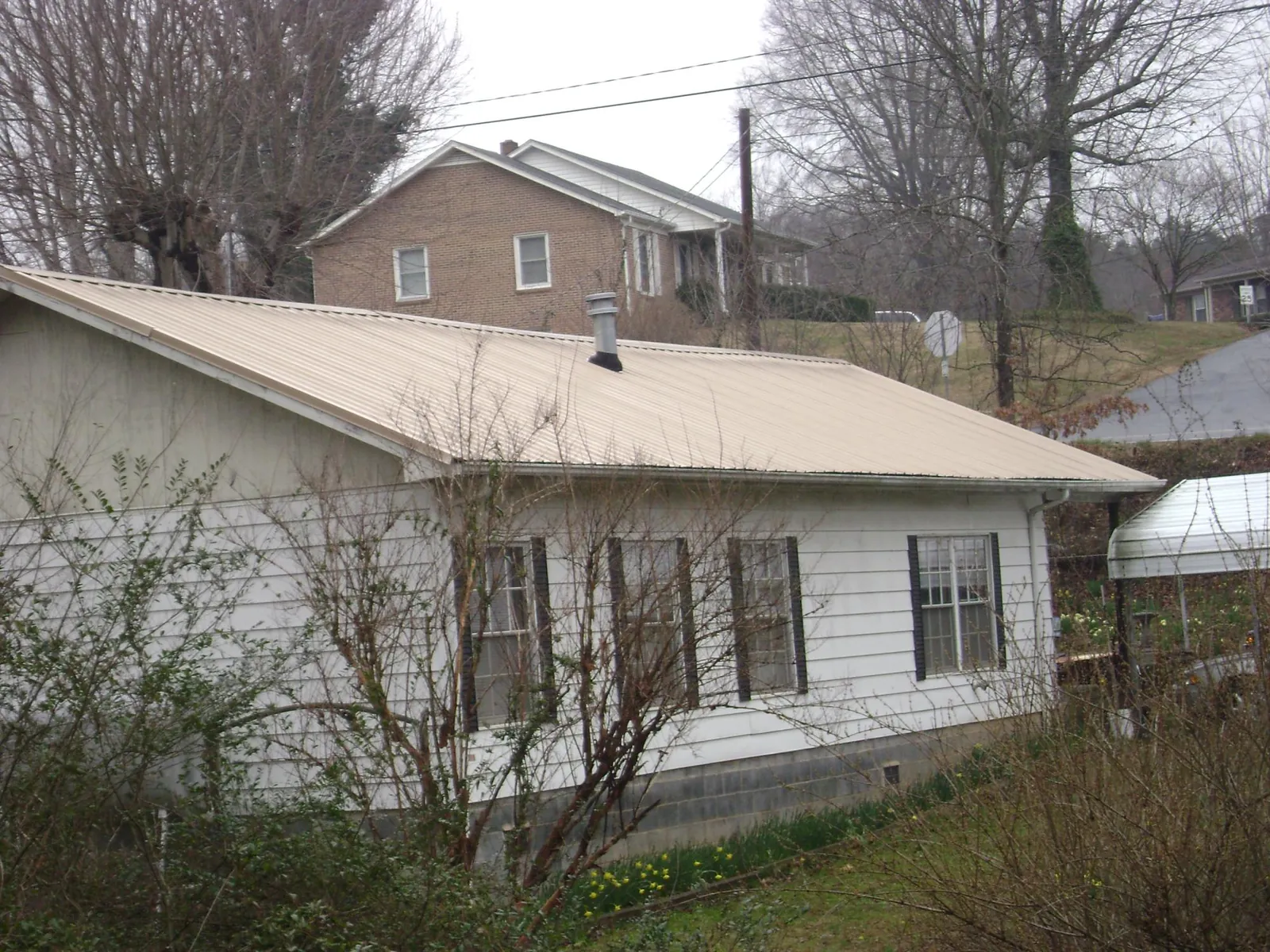 Tan metal roof on a white sided house set into a hillside — Commercial Roofing by Roofing Brothers in North Tonawanda